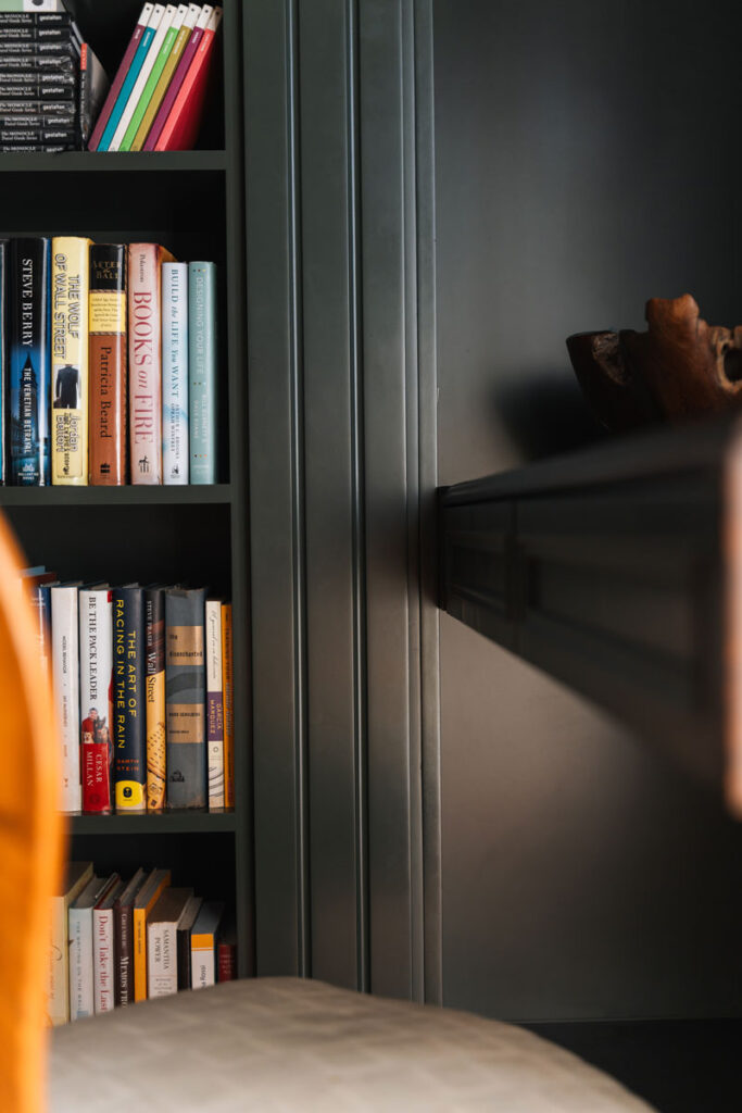 Detalle de repisas con libros de diseno y negocios, puerta corrediza cerrada y escultura en raiz de madera.