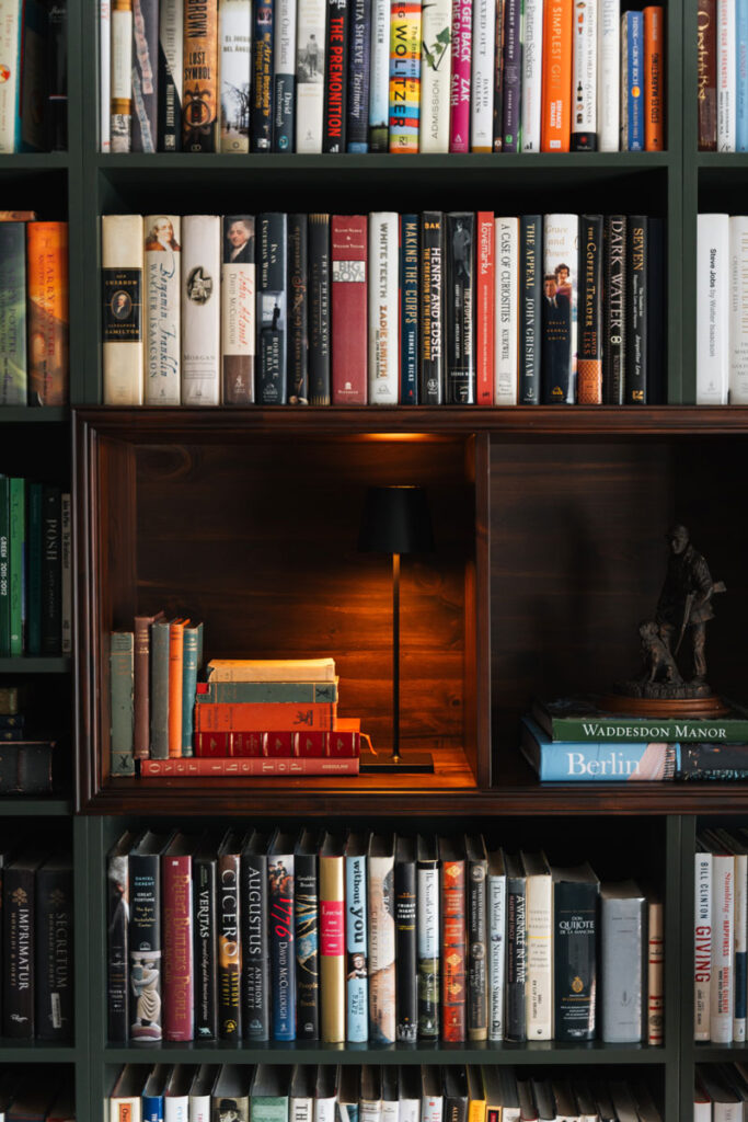 Detalle de nicho iluminado en la biblioteca con lampara de mesa, libros de tapa dura y escultura de bronce.