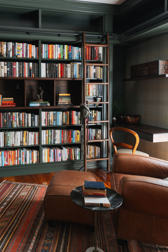 Rincon de lectura en la biblioteca con sillon y otomana de cuero cafe, mesa auxiliar de marmol negro y alfombra kilim.
