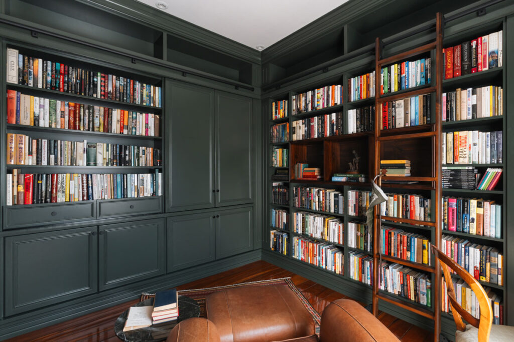 Biblioteca de piso a techo en verde bosque con escalera corrediza de madera, sillon de cuero y mesa de centro, en una residencia de Pinares, Curridabat.